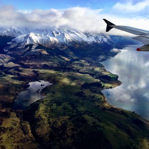 A stunning view of the landscape of a lake, rolling green hills and snow capped mountains as the plane arrives into Queenstown, NZ