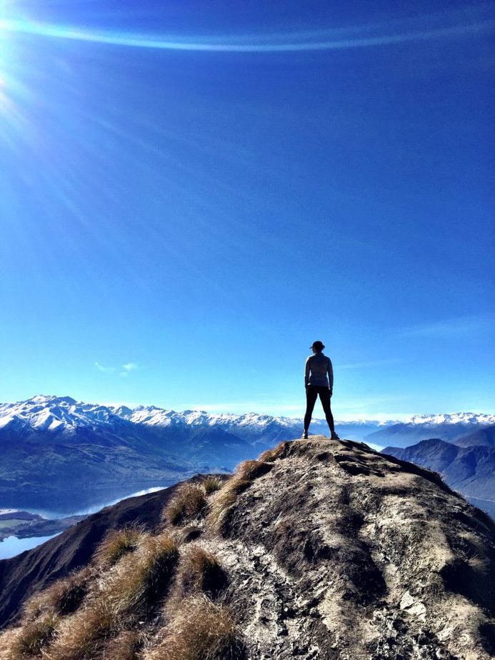 Distant shot of Tayler standing on the top of Roy's Peak in Wanaka, New Zealand overlooking the beautiful mountain landscape