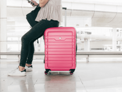 Woman sits on her pink suitcase in the airport