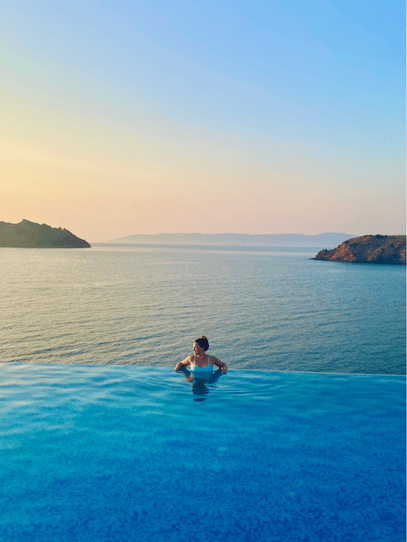 A woman casually stands in an infinity pool looking over her shoulder with the sea in the background